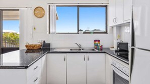 A modern kitchen with white cabinets, a black countertop, a built-in oven, and a window with curtains.