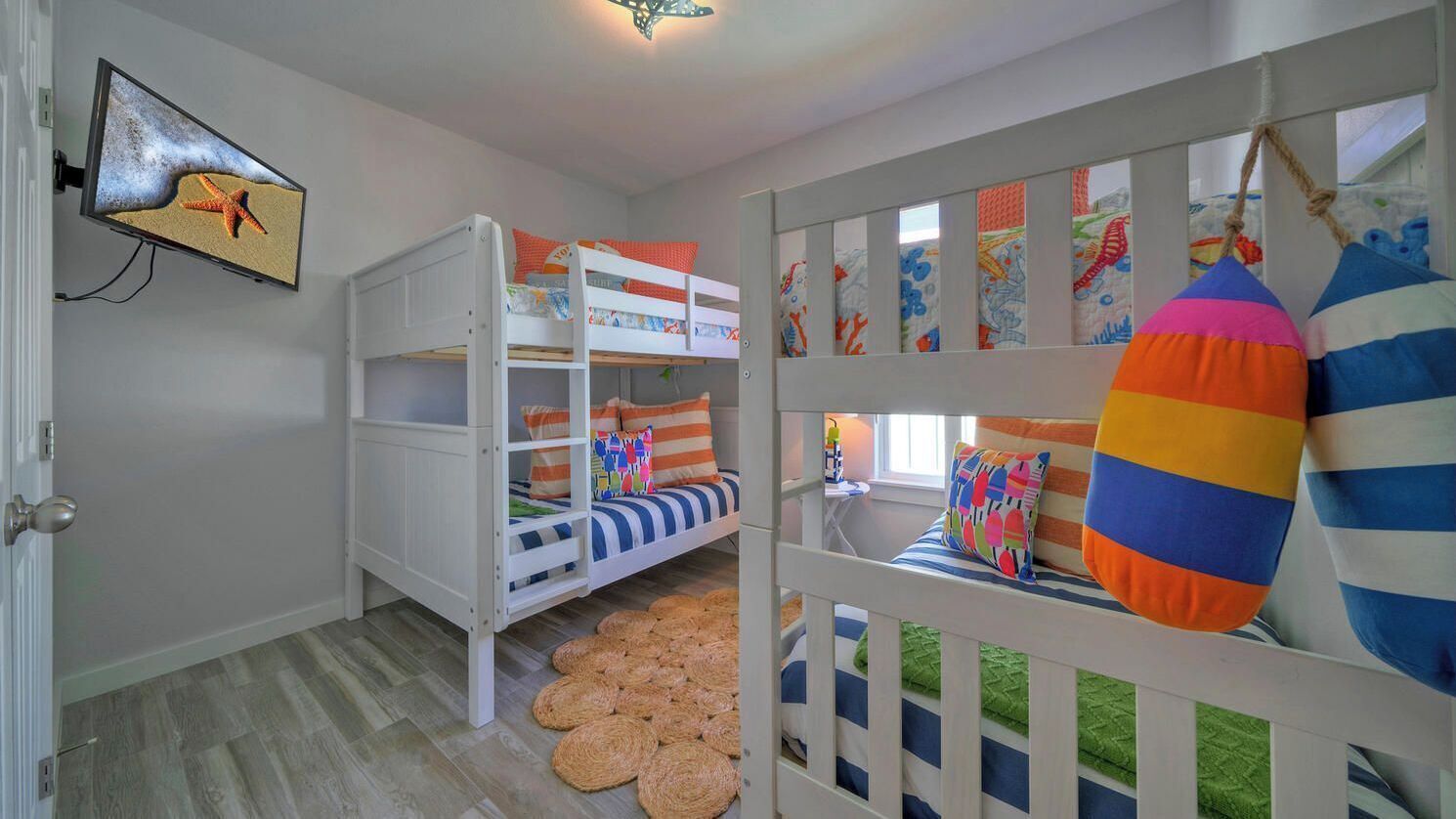 Un lit superposé pour enfants avec une literie à rayures, un téléviseur fixé au mur et une décoration murale colorée.