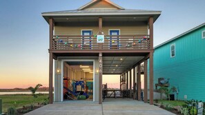 A building with a covered entrance, a balcony with colorful decorations, and a slide. - Pelican's Porch by Avantstay Private Pool, Views (Port Aransas)