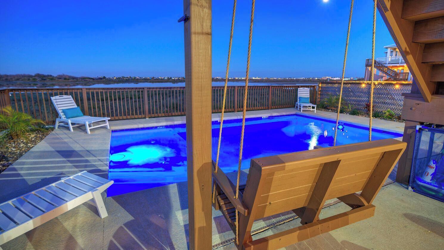 Un área de piscina con una silla colgante, una tumbona y una terraza de madera.