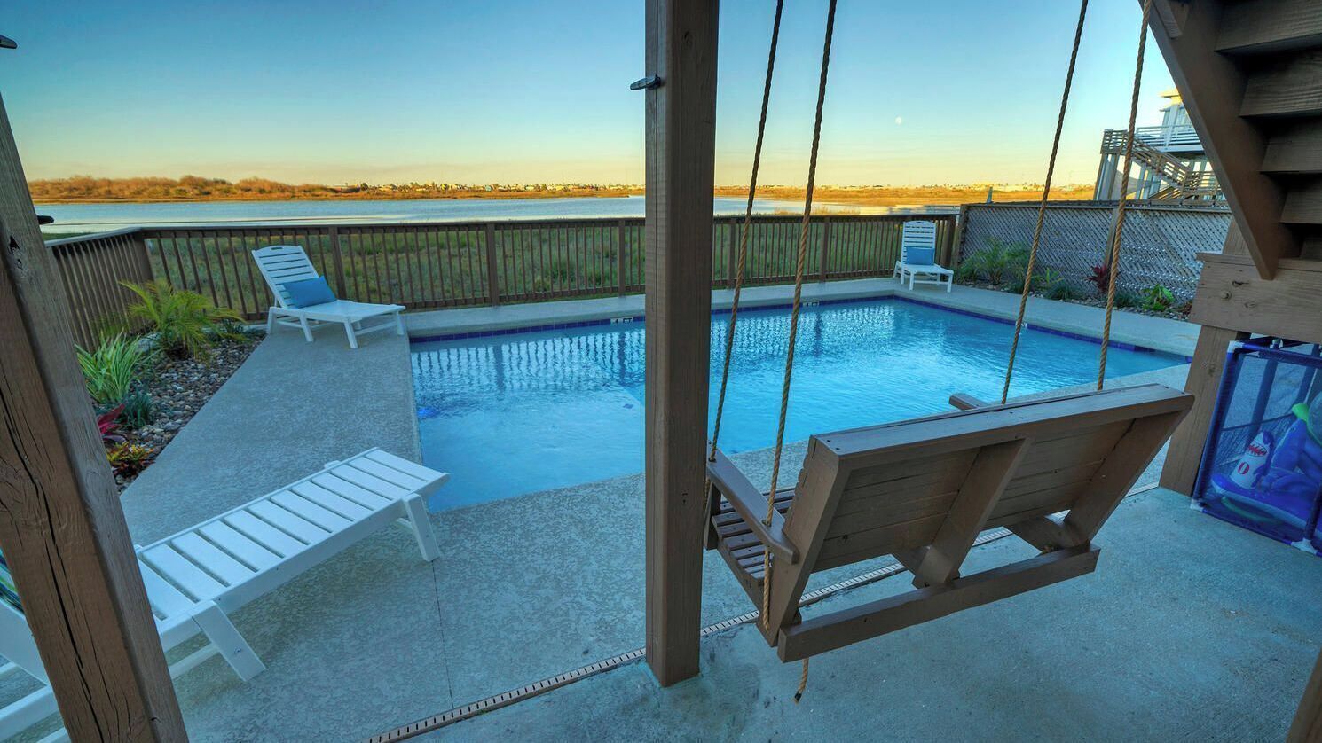 A backyard with a swimming pool, a swing, and a view of the beach.