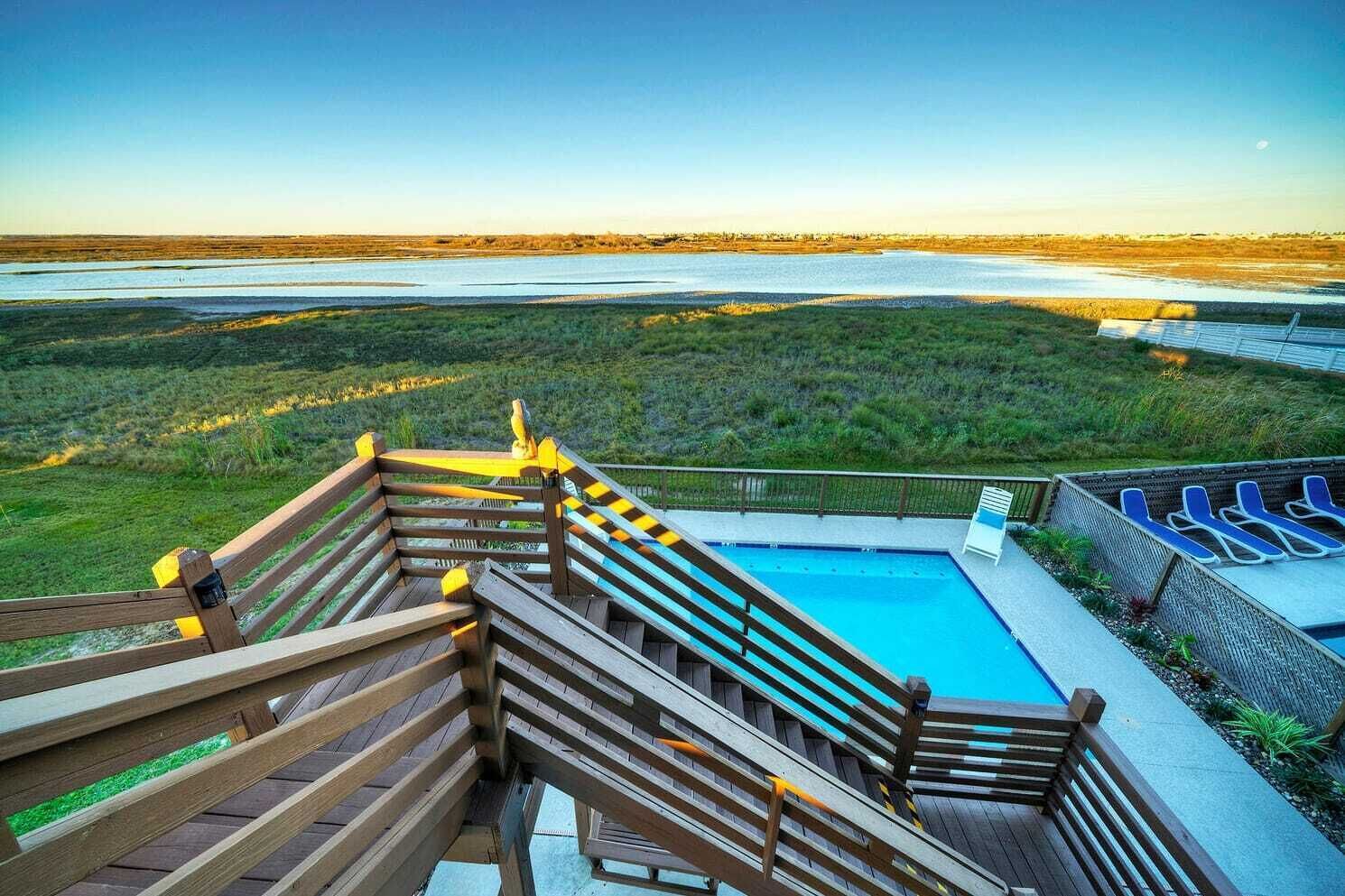 Terraza de madera con piscina y sillones de descanso con vistas a la playa.