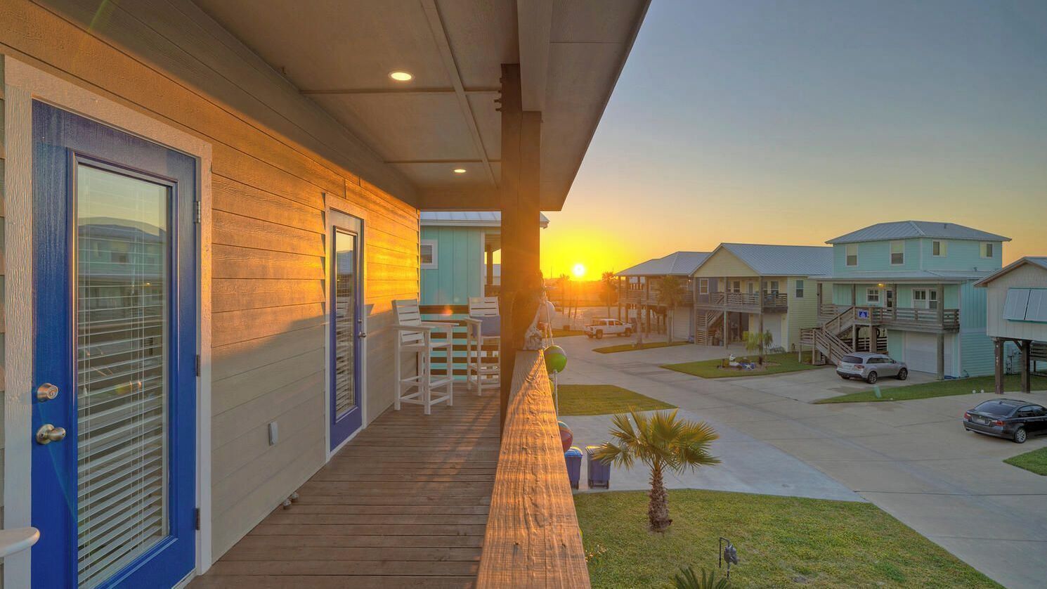 Un immeuble résidentiel doté d’une terrasse en bois, d’un porche couvert et offrant une vue sur les maisons voisines au coucher du soleil.