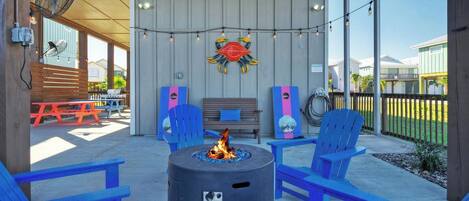 An outdoor seating area with a fire pit, blue chairs, and a wooden bench.