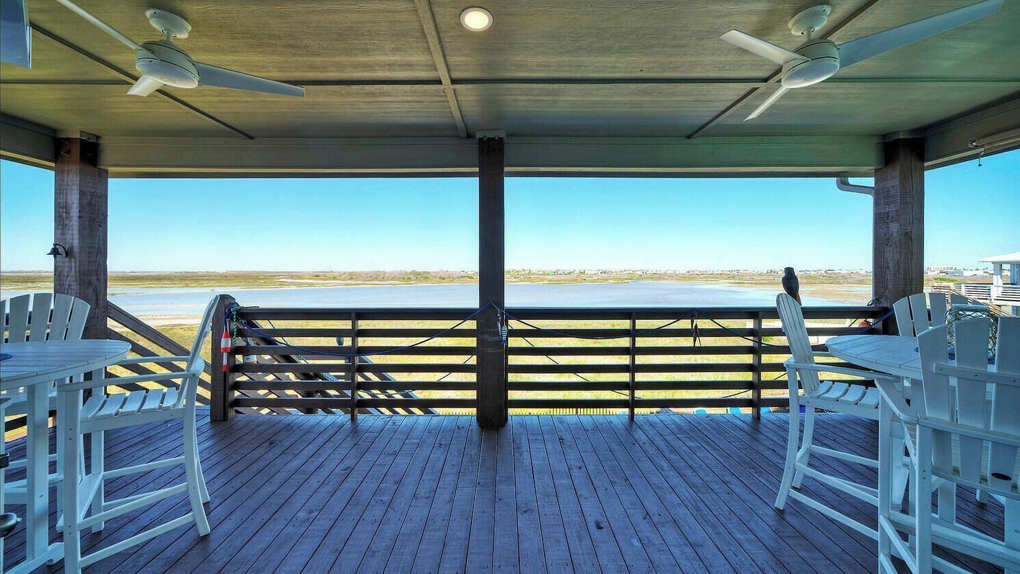 Eine Außenterrasse mit Blick auf den Strand, Holzstühle, Tische und Deckenventilatoren.