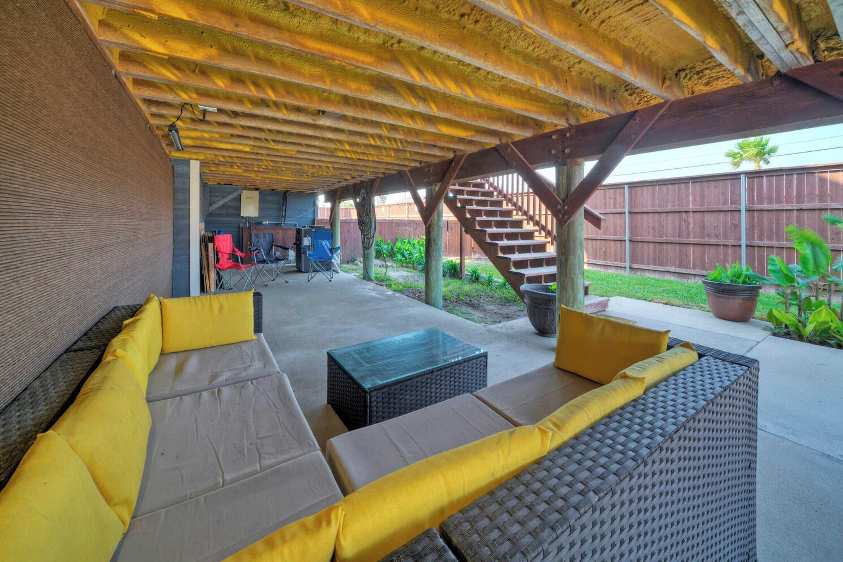 An outdoor patio area with a covered seating area, a staircase, and a view of a backyard.