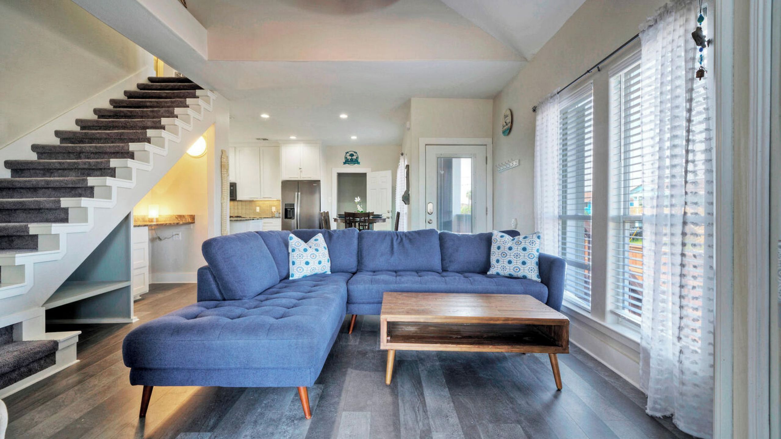 A modern living room with a sectional sofa, a wooden coffee table, and a staircase.