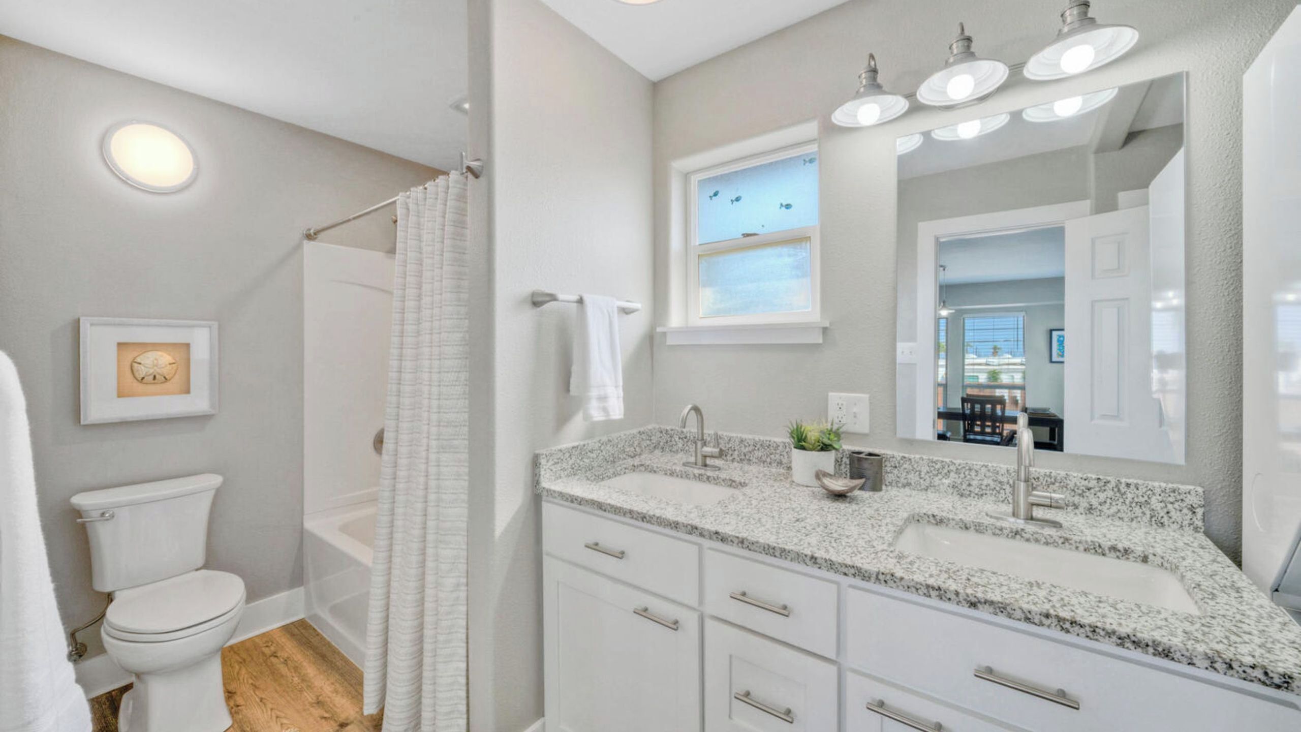 A bathroom with a toilet, shower, sink, and a large mirror.
