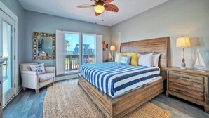 A bedroom with a large bed, wooden headboard, a nightstand, a chair, a ceiling fan, and a view through a sliding door to the outside. - Makaira Azul by Avantstay Pool & Putting Green! (Port Aransas)