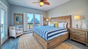 A bedroom with a large bed, wooden headboard, a nightstand, a chair, a ceiling fan, and a view through a sliding door to the outside.