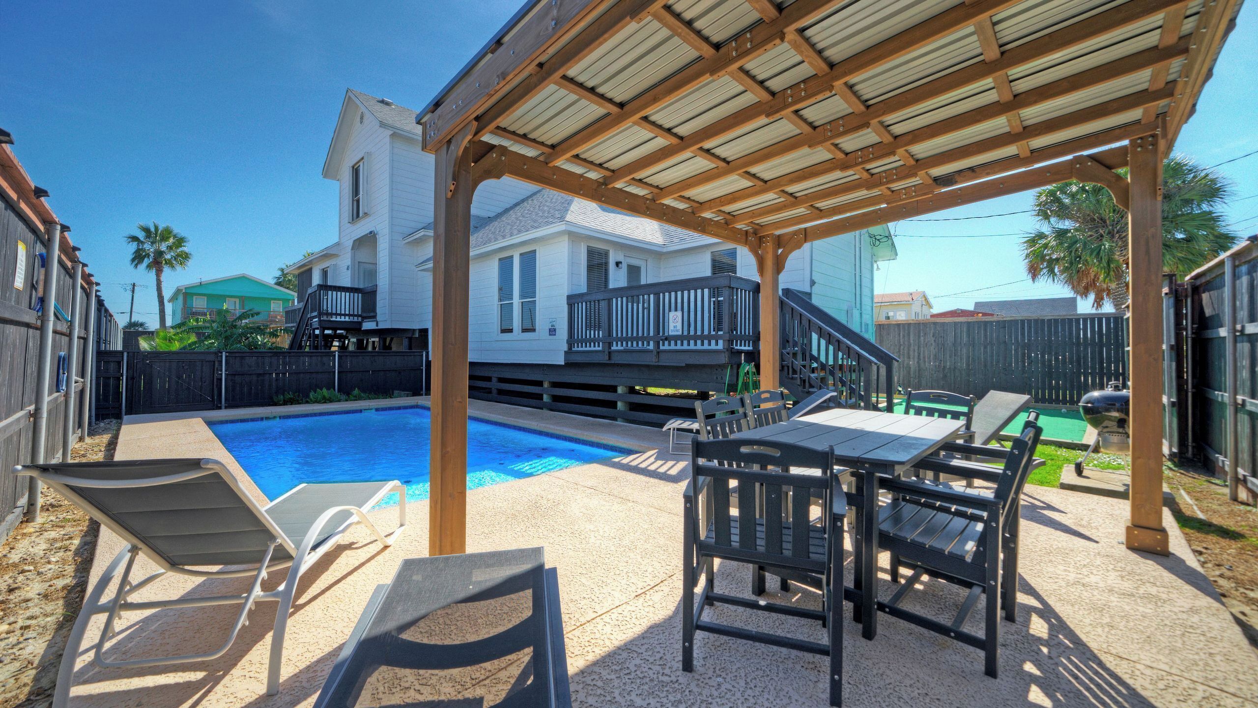 A covered patio with a pool, outdoor furniture, and a wooden pergola.