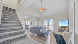 A spacious living area with a staircase, a large sectional sofa, a flat-screen TV, and a dining area. - Makaira Azul by Avantstay Pool & Putting Green! (Port Aransas)