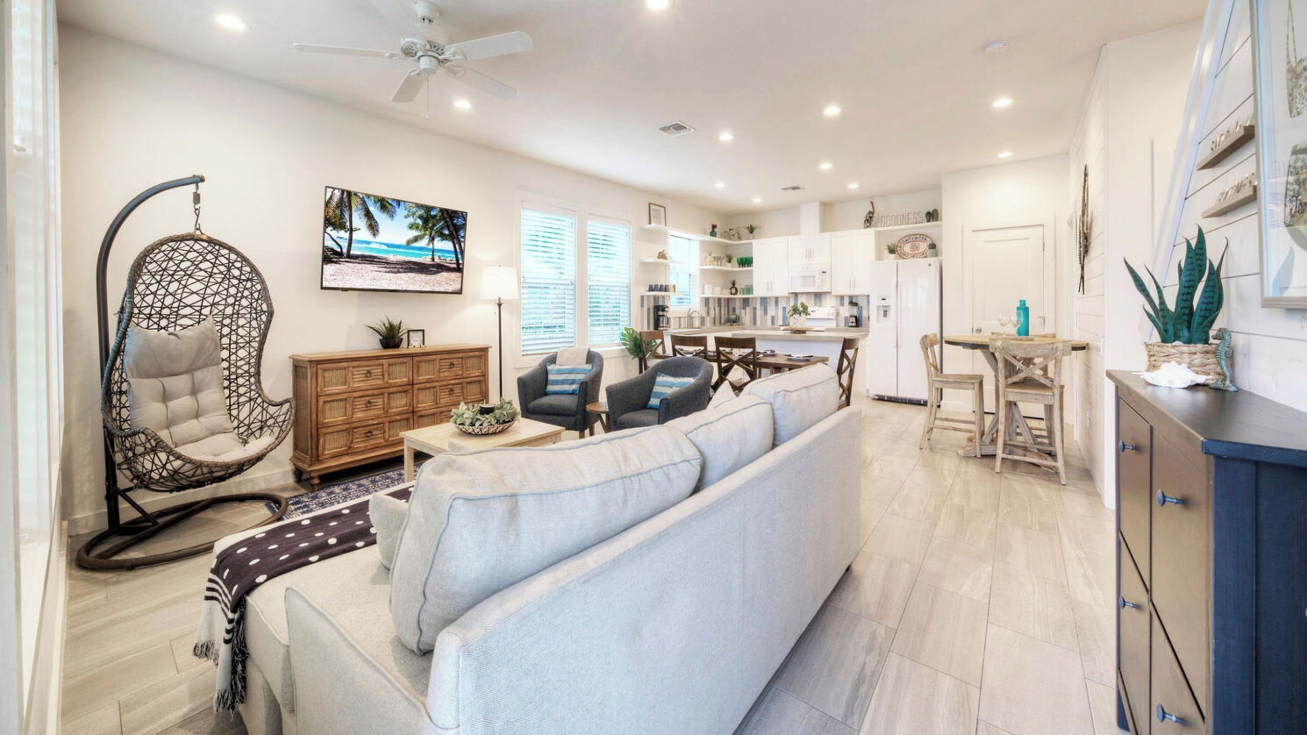 A modern living room with a sofa, a hanging chair, and a kitchen area with white cabinets and a dining table.