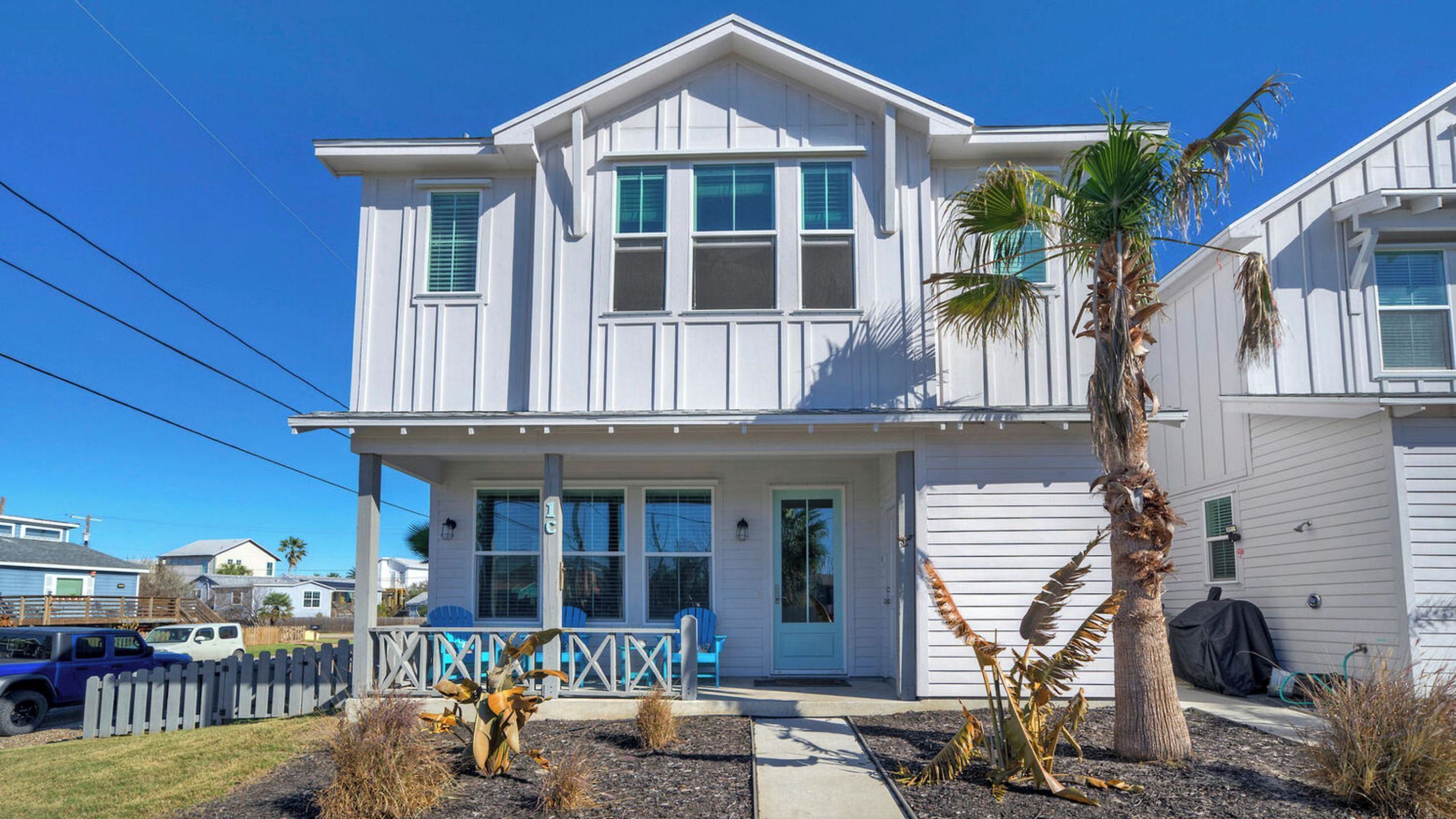 A two-story house with a porch, a garage, and a small garden with plants and a palm tree.