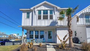 A two-story house with a porch, a garage, and a small garden with plants and a palm tree. - Newly Built, Pool, Walk to Old Town Eats+marina Shorely Goodness by Avantstay (Port Aransas)