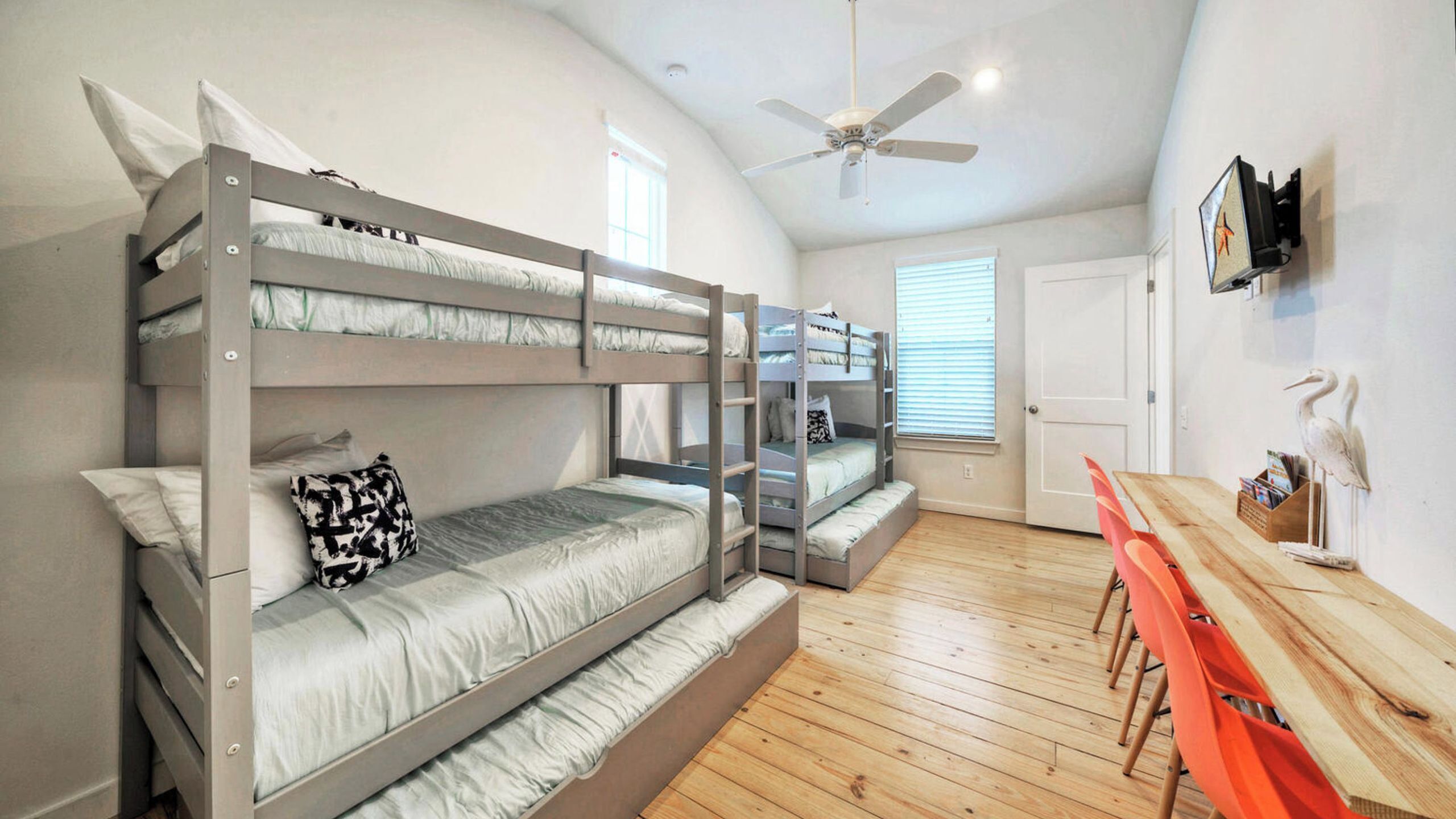 Une chambre avec un lit superposé, un ventilateur de plafond, une table en bois et une porte.