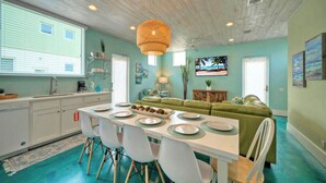 A kitchen with a dining table set for six, a green sofa, and a large window. - Rooftop Patio w/ View, Pool, Near the Beach Lost Shaker of Salt by Avantstay (Port Aransas)