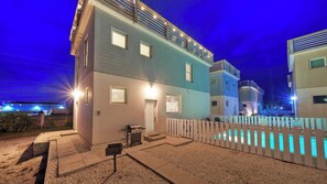 Um edifício de vários andares com piscina, área para churrasco e cerca branca de piquete.