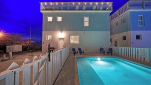 Um edifício de dois andares com piscina, um deck cercado e duas cadeiras.