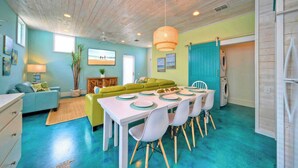 A dining area with a table set for four, a green sofa, and a ceiling fan. - Rooftop Patio w/ View, Pool, Near the Beach Lost Shaker of Salt by Avantstay (Port Aransas)