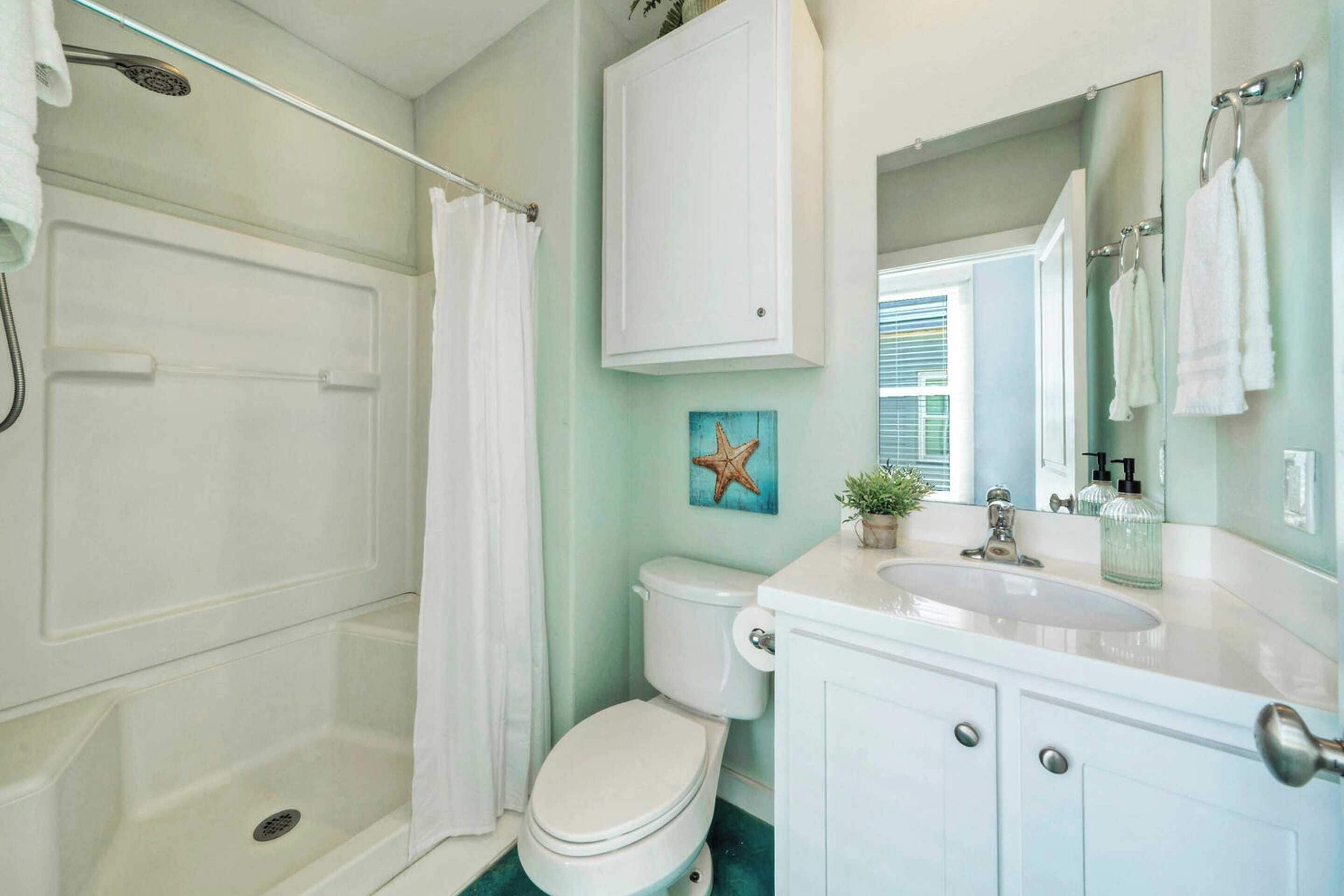 A bathroom with a shower, toilet, sink, and cabinet.