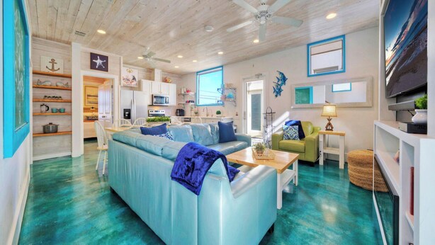 A living room with a blue sofa, a wooden ceiling, and a kitchen area. - Stella Maris by Avantstay Rooftop View + Pool (Port Aransas)