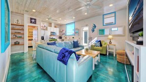 A living room with a blue sofa, a wooden ceiling, and a kitchen area. - Stella Maris by Avantstay Rooftop View + Pool (Port Aransas)
