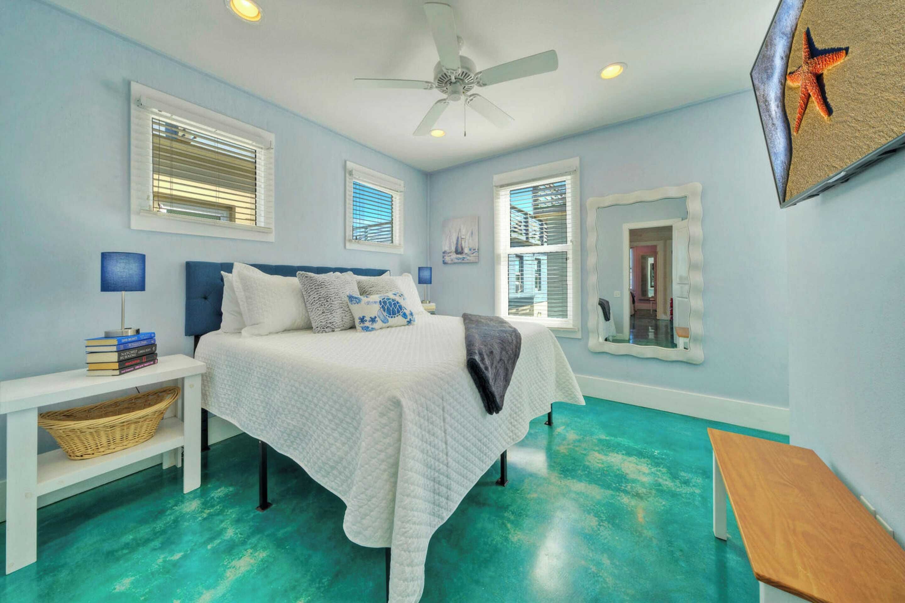 A bedroom with a bed, bedside tables, a ceiling fan, and large windows with blinds.