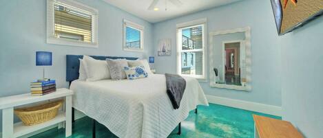A bedroom with a bed, bedside tables, a ceiling fan, and large windows with blinds.