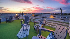 A patio with Adirondack chairs and tables, overlooking a road with vehicles. - Stella Maris by Avantstay Rooftop View + Pool (Port Aransas)