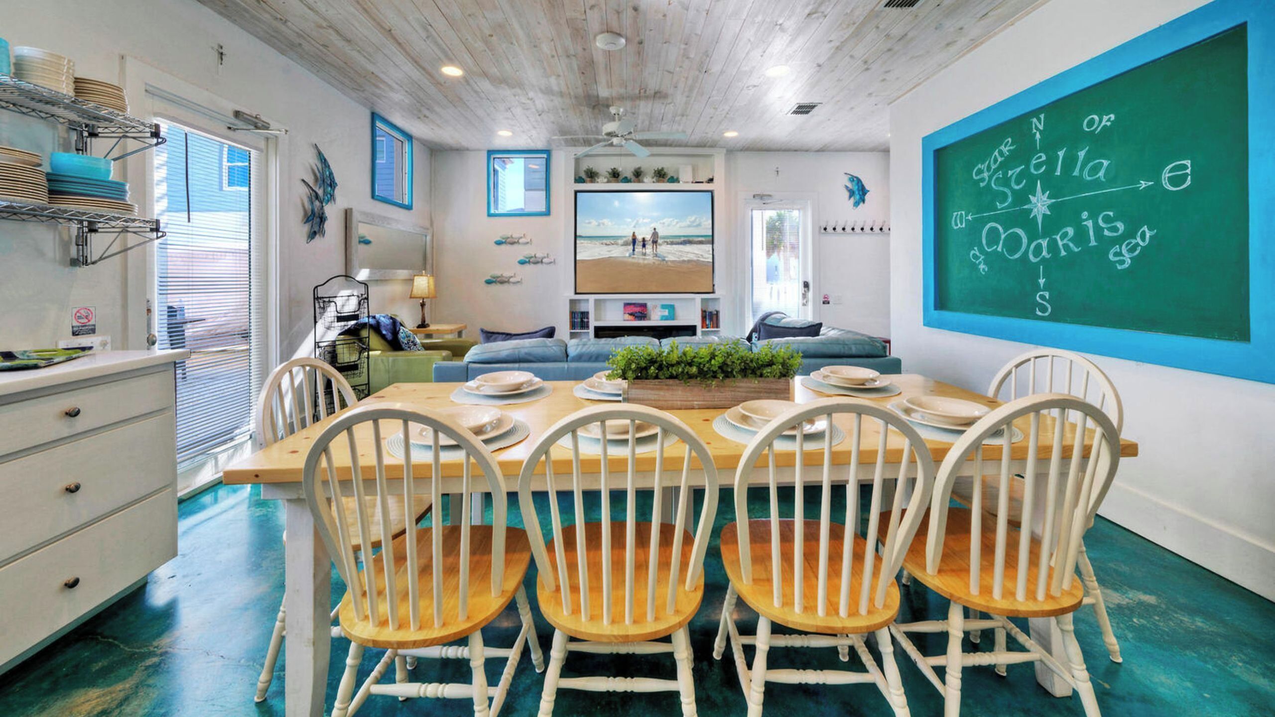 A dining area with a wooden table, white chairs, and a green chalkboard with writing.