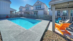 A swimming pool with a wooden deck, surrounded by a white fence and houses in the background. - Breakaway by Avantstay Near Music, Eats (Port Aransas)