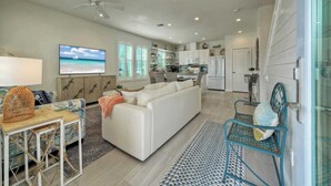 A modern living room with a white sofa, a TV, and a dining area with a table and chairs. - Breakaway by Avantstay Near Music, Eats (Port Aransas)