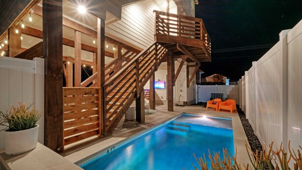 A pool area with a wooden staircase leading to a deck, surrounded by white walls and potted plants. - Seas The Bay by Avantstay In-town Private Pool (Port Aransas)