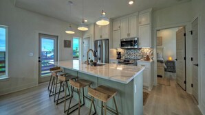 A modern kitchen with a large island, bar stools, and stainless steel appliances. - Seas The Bay by Avantstay In-town Private Pool (Port Aransas)