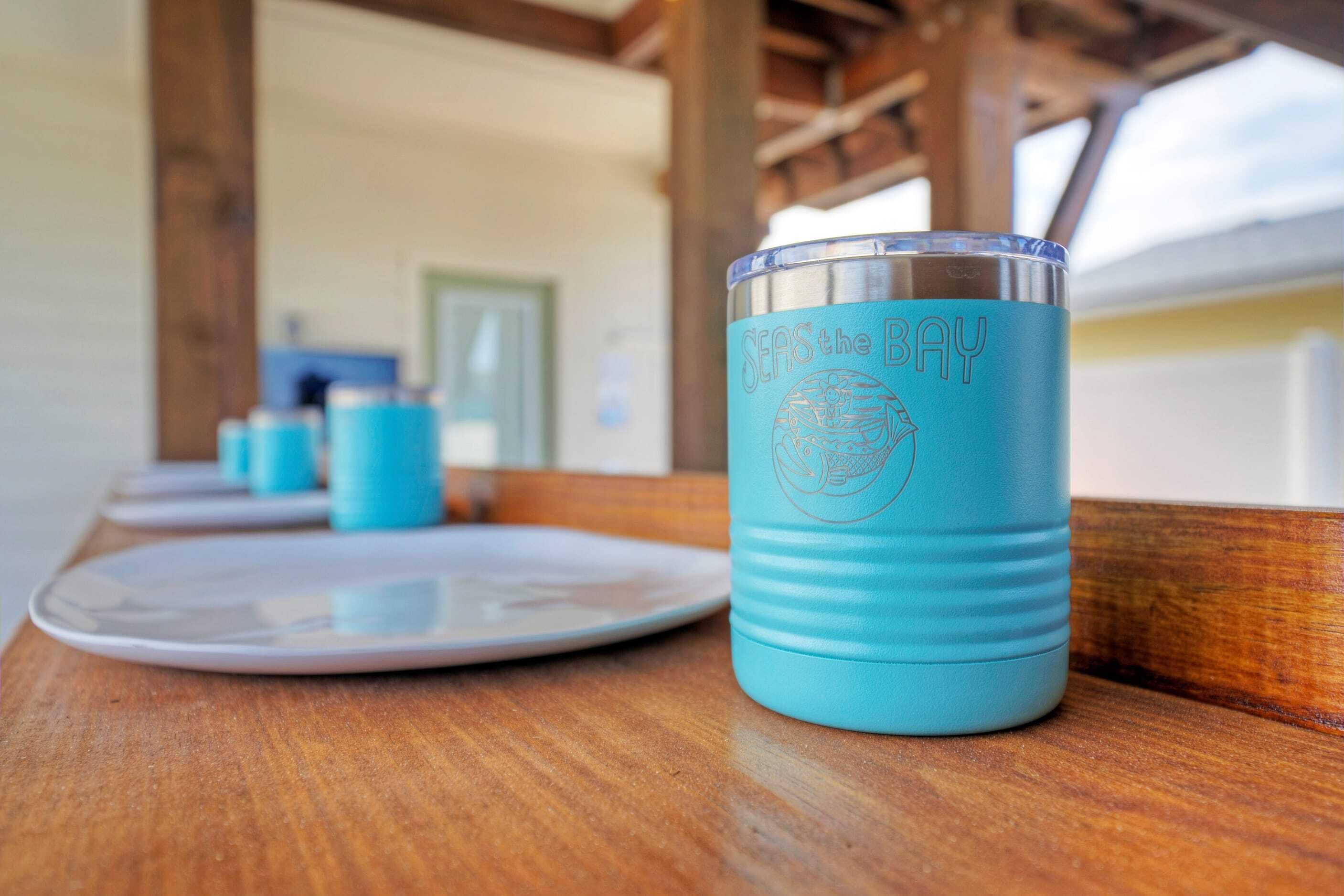 Ein türkisfarbenes Glas mit dem Aufdruck „SEAS the BAY“ und einem Logo auf einem Holztisch.