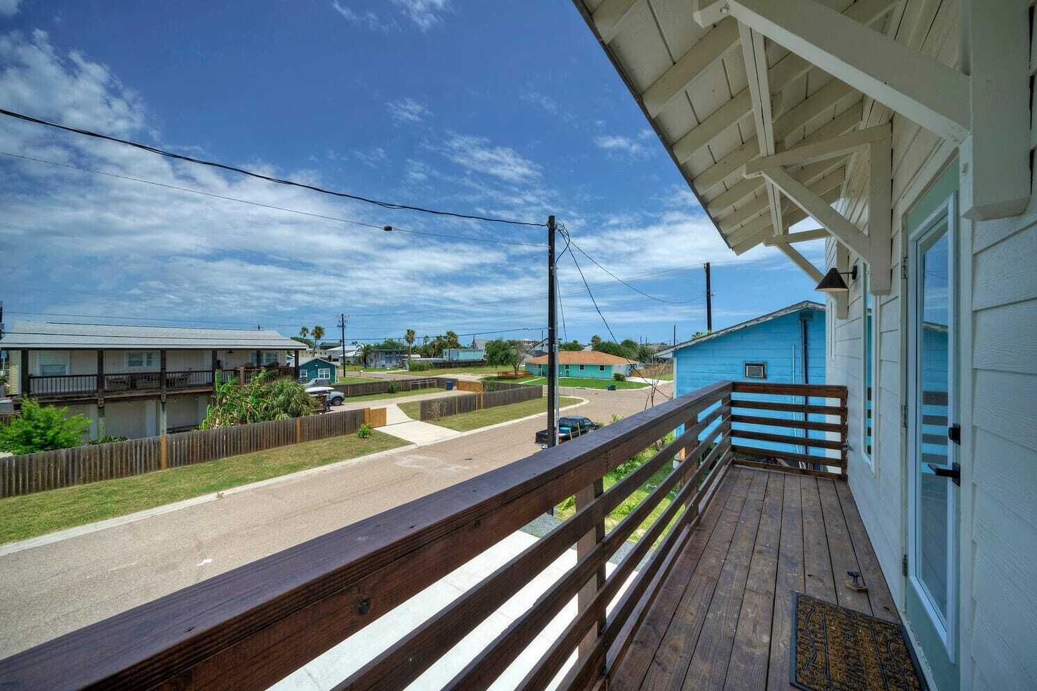 A wooden deck with a railing overlooking a street and houses.