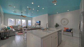 A modern kitchen with a central island, white cabinetry, and a blue ceiling. - Pool Access, Private Patio Living, Near the Beach Seahorse Cove by Avantstay (Port Aransas)