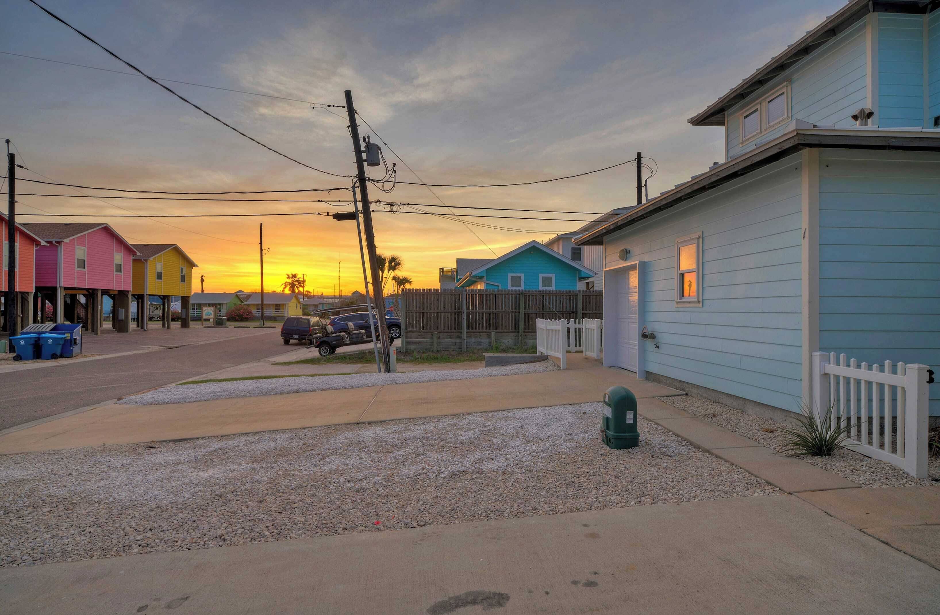 A residential street with colorful houses, a gravel driveway, and a parked car.
