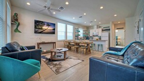 A modern living room with a sofa, a coffee table, and a dining area with chairs and a table. - A Crazy Beach by Avantstay Steps to Old Town (Port Aransas)