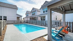 Une piscine avec une terrasse en bois, un espace salon couvert et une clôture blanche.