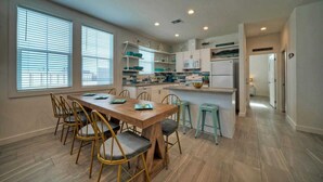 A modern kitchen with a dining area, featuring a wooden table, chairs, and a small island with stools. - A Crazy Beach by Avantstay Steps to Old Town (Port Aransas)