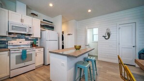 A modern kitchen with white cabinetry, a central island with stools, a microwave, stove, and refrigerator. - A Crazy Beach by Avantstay Steps to Old Town (Port Aransas)