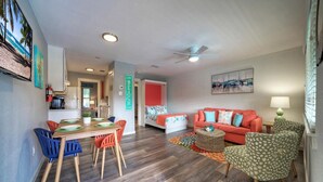 A modern living room with a red sofa, a dining area with colorful chairs, and a kitchen in the background.
