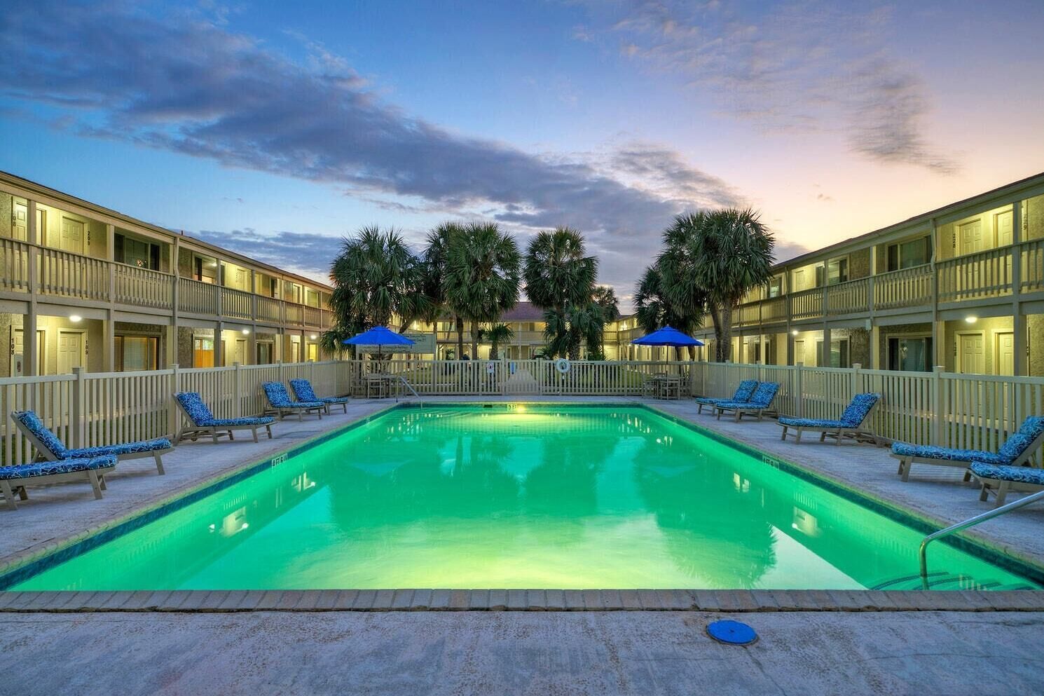 A swimming pool with lounge chairs and umbrellas, surrounded by a building with balconies.
