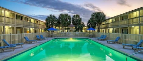 A swimming pool with lounge chairs and umbrellas, surrounded by a building with balconies.