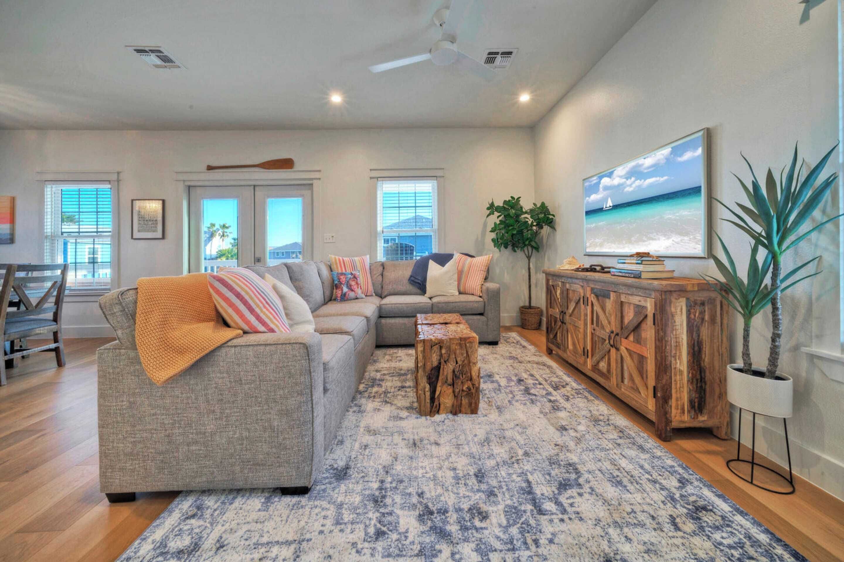 Un salón con un sofá gris, una mesa de centro, un mueble de madera y un cuadro grande con una playa.
