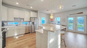 A modern kitchen with white cabinetry, a central island, and a dining area with a view. - Priv Pool & Yard w/ Putting Green! Newly Remodeled Always Sunny by Avantstay (Port Aransas)