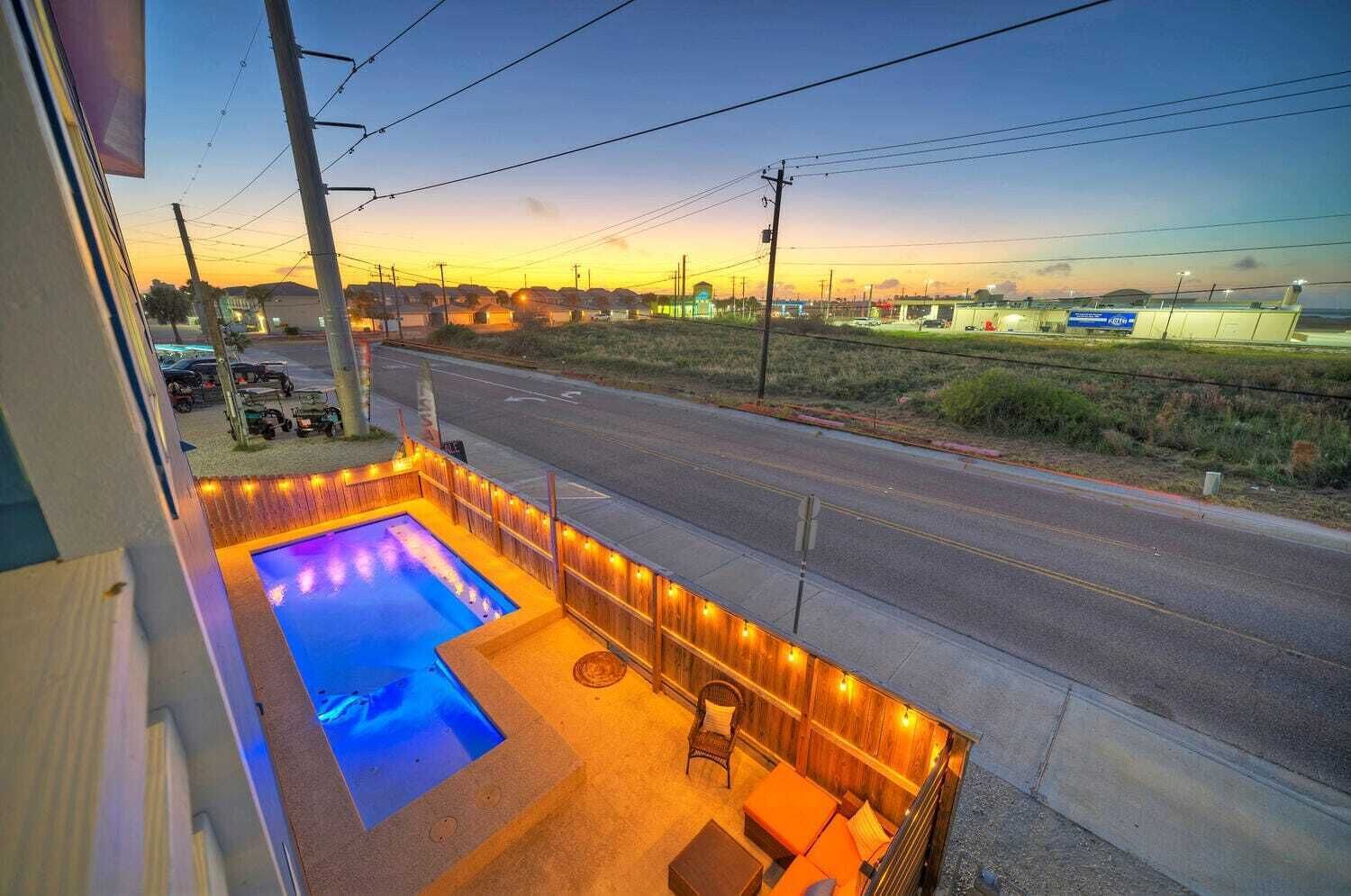 A rooftop pool with a view of a road and distant buildings during sunset.
