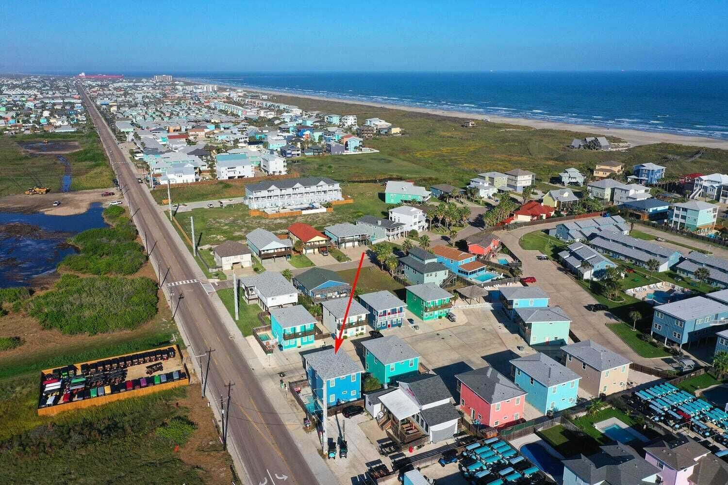 An aerial view of a coastal residential area with houses, a road, and a beach.